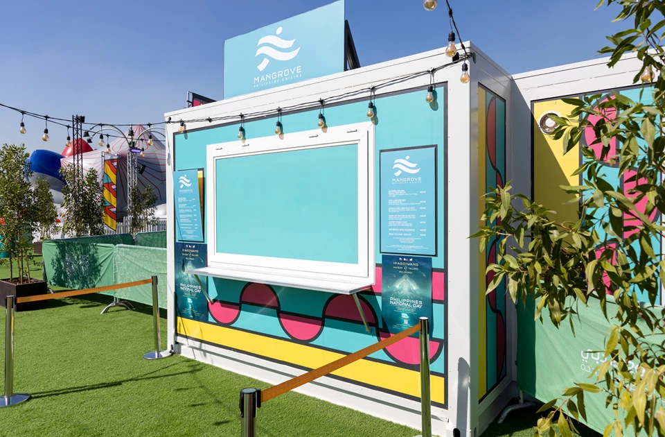 Brightly coloured temporary kitchen structure featuring turquoise and pink design elements, set against a clear sky.