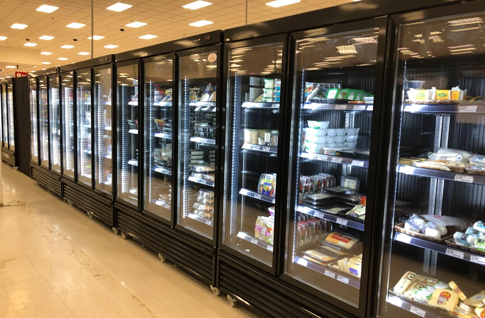 Five black-framed refrigerated display units filled with various packaged products under bright lighting.