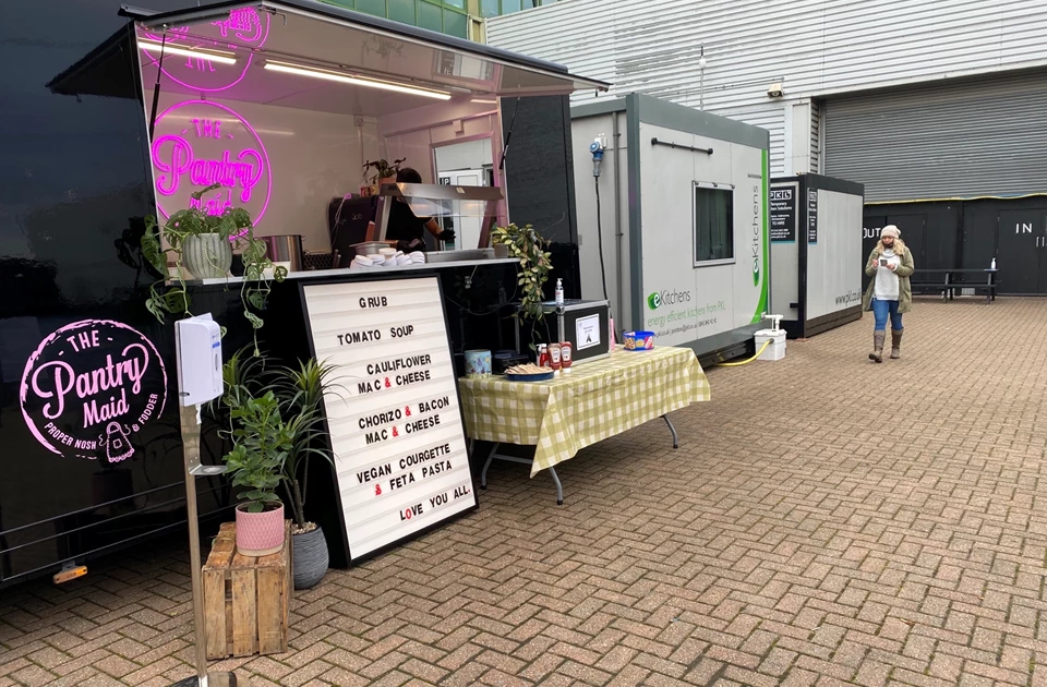 Temporary kitchen setup featuring a pink-lit food stall and a checkered tablecloth with signage.
