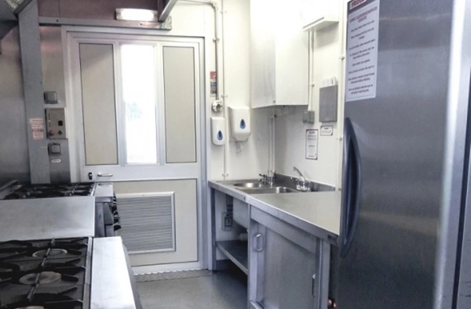 Modern field kitchen interior featuring stainless steel surfaces and a white door, well-lit environment.