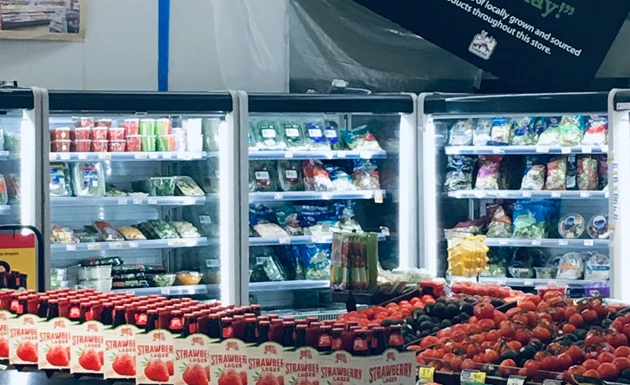 Refrigerated display with various packaged vegetables and fruits, featuring bright red tomatoes in foreground.