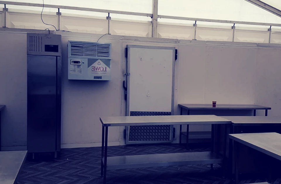 A clean, empty kitchen space with stainless steel tables and a large white refrigerator.