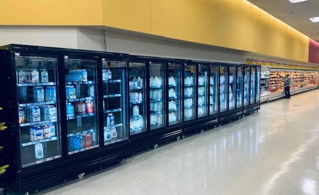 Row of black refrigeration units displaying various beverages against a yellow wall.