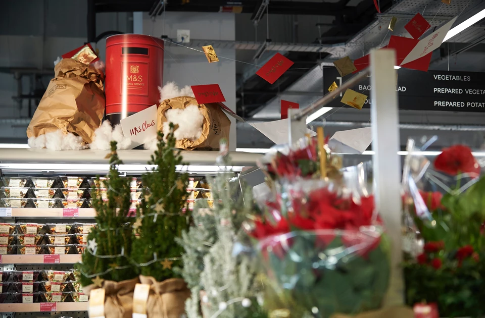 Christmas decorations and greenery displayed on shelves, featuring red and green colours in a retail setting.