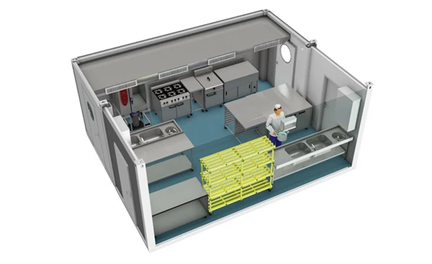 A temporary kitchen layout featuring stainless steel equipment and blue flooring, with a worker present.