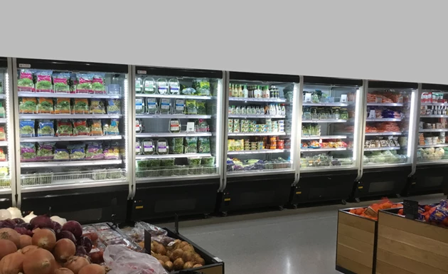 Refrigerated display units filled with various packaged foods, alongside a wooden crate of fresh produce.