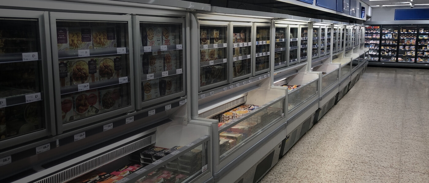 Chilled grocery display featuring glass-fronted freezers and a variety of packaged food items.