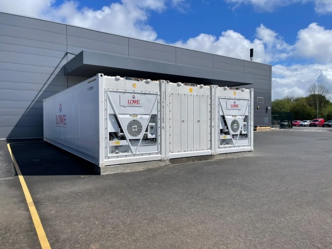 White containerised cold storage unit with ventilation systems against a clear blue sky.