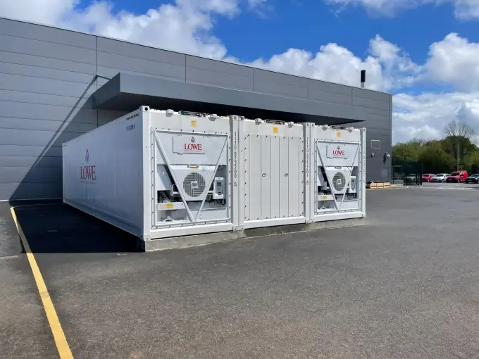 White containerised cold storage unit with ventilation systems against a clear blue sky.