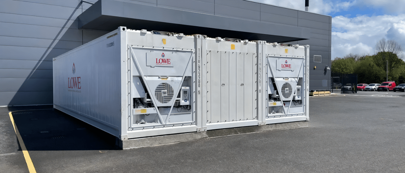 White containerised 2 bay cold storage unit with visible air conditioning units, set against a grey building.