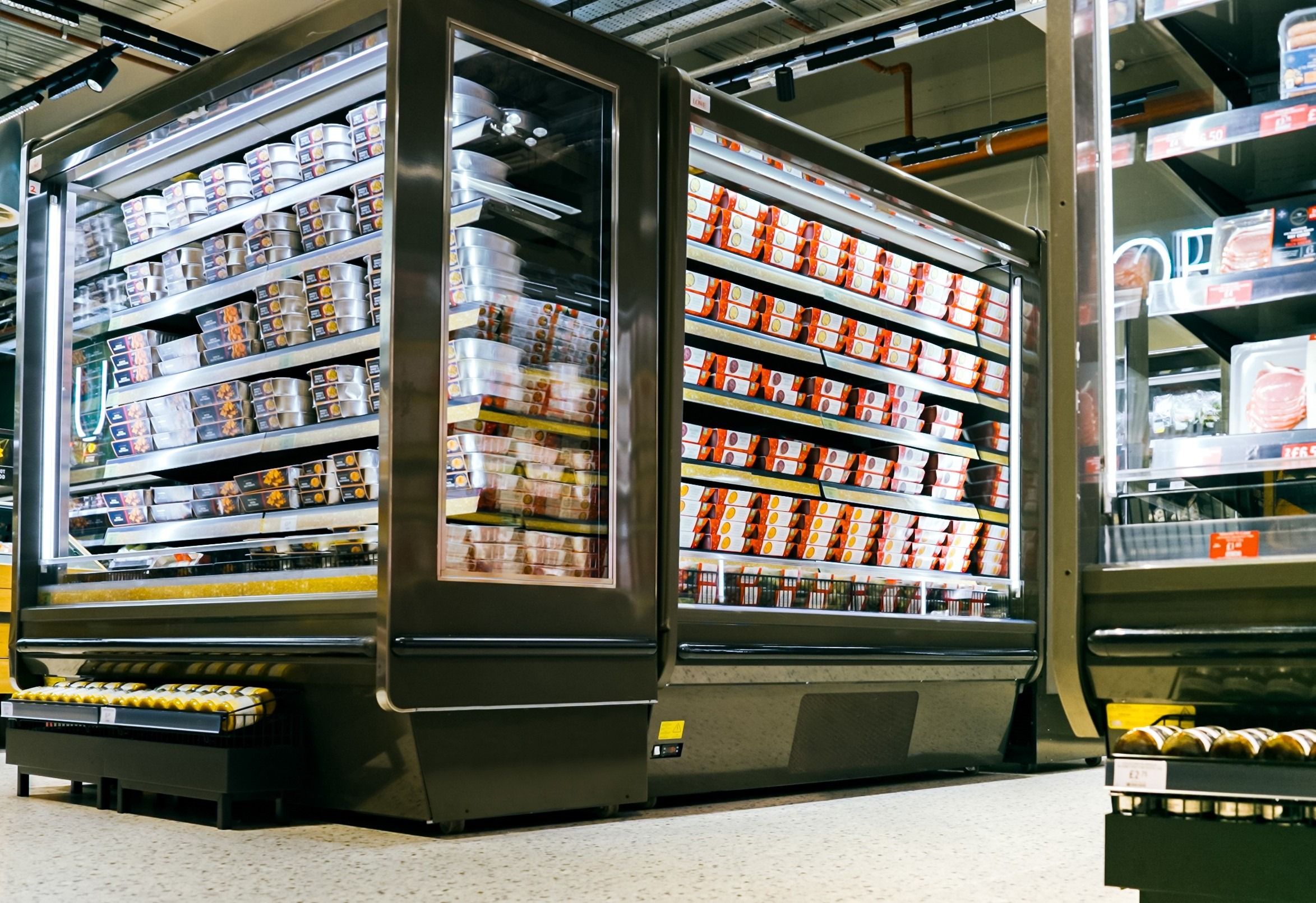 Chilled display cabinet filled with various food containers, featuring a sleek black exterior and bright packaging.