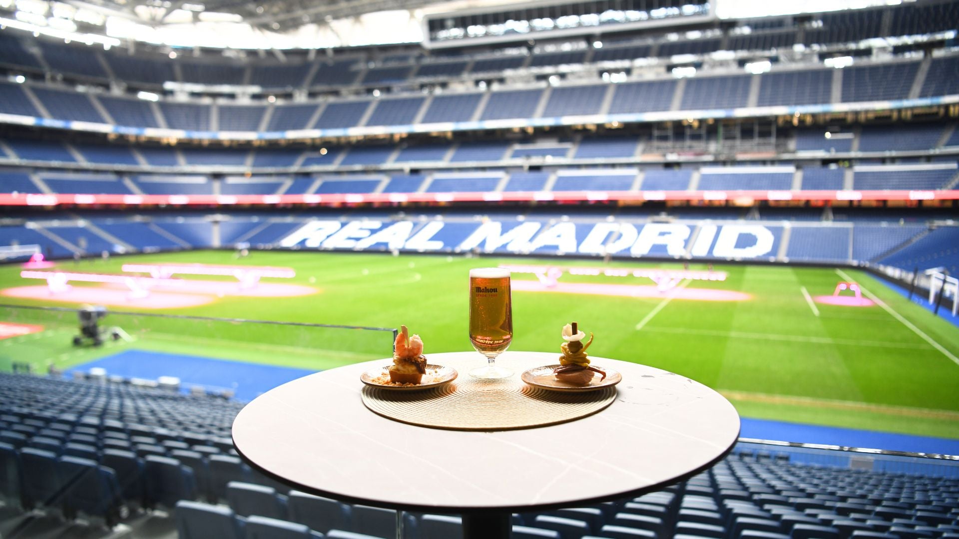 Table set with two desserts and a drink, overlooking the green pitch at Real Madrid stadium.