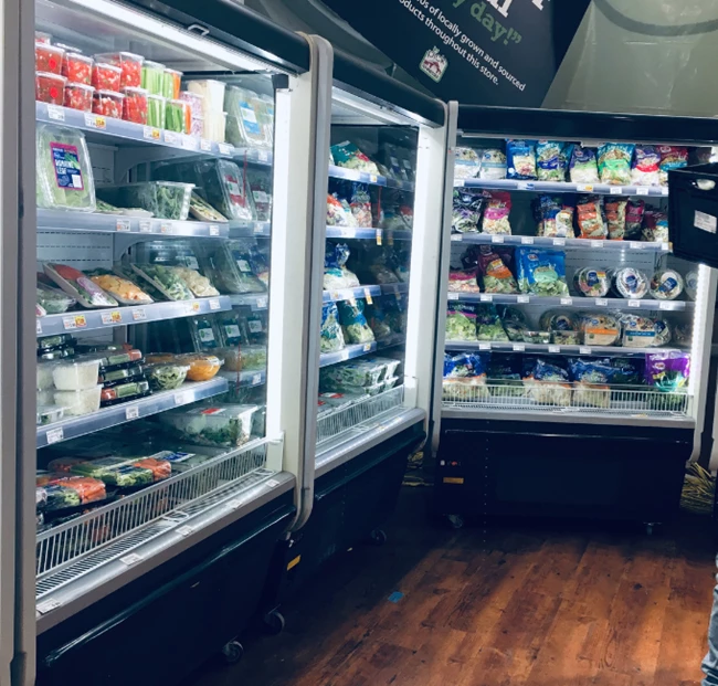 Refrigerated display units filled with various packaged food items, set against a wooden floor.