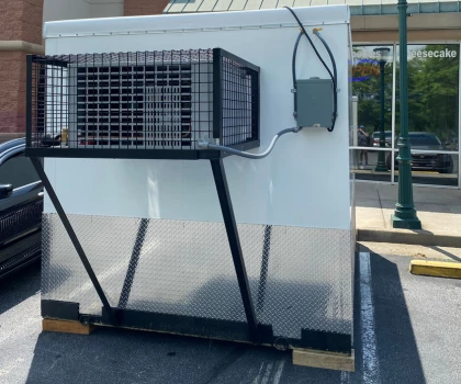 Large white air conditioning unit with a metal frame, positioned on a concrete surface.