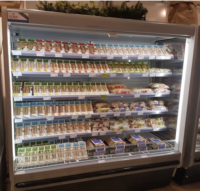 Refrigerated display case filled with various dairy products, featuring predominantly white and green packaging.