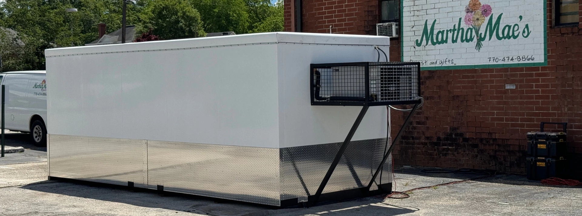 Large white storage unit with a shiny silver base, positioned against a brick wall.
