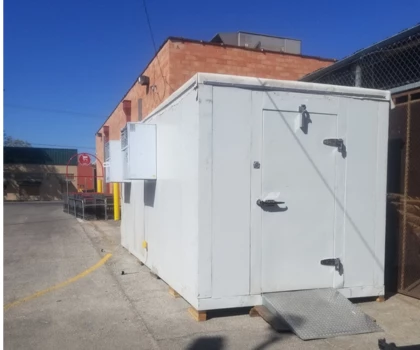 White storage unit with a ramp, set against a clear blue sky and brick building backdrop.
