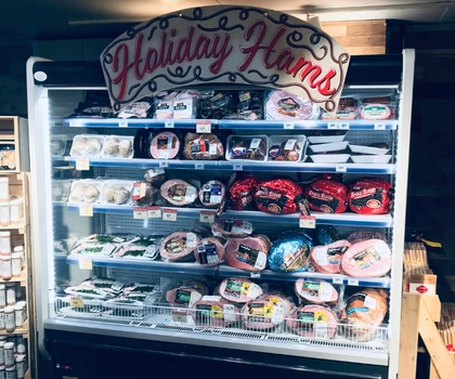 Display case filled with various holiday hams, featuring vibrant packaging and a decorative sign above.