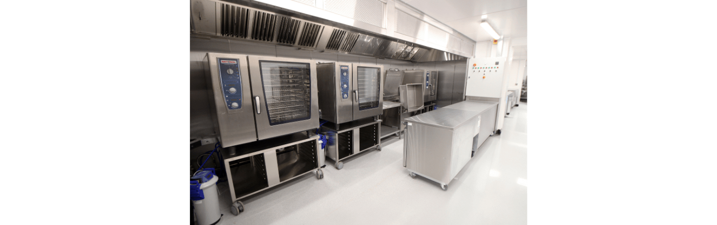Modern stainless steel kitchen equipment, including ovens and a mobile worktable, in a bright environment.