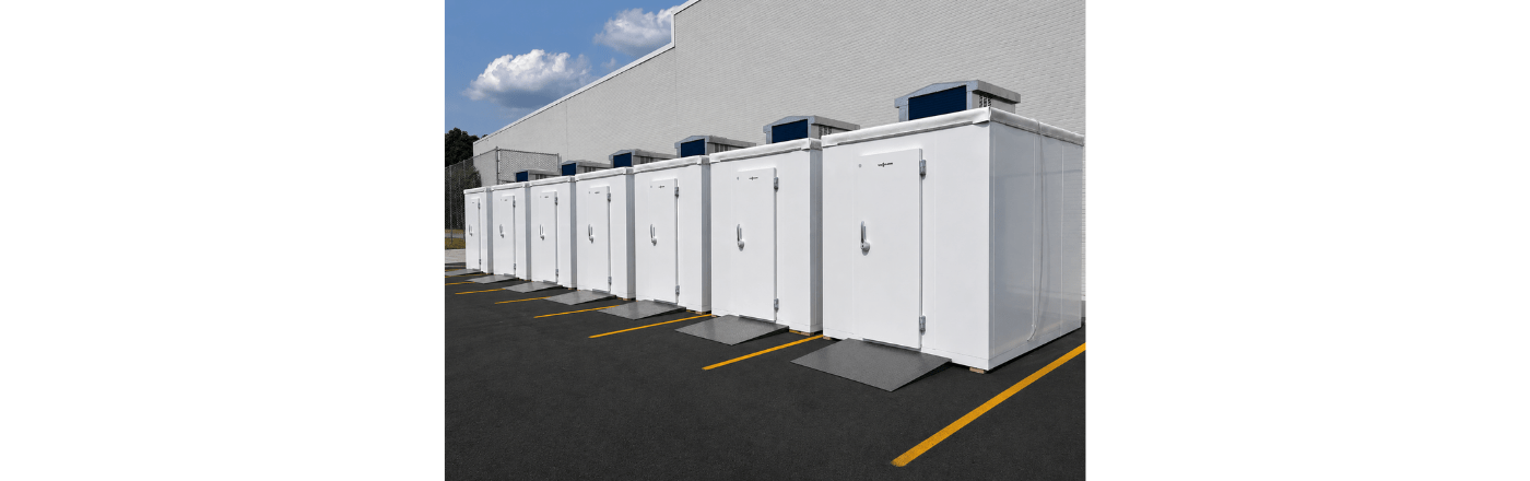 Five white storage units lined up against a grey wall, with a clear blue sky above.