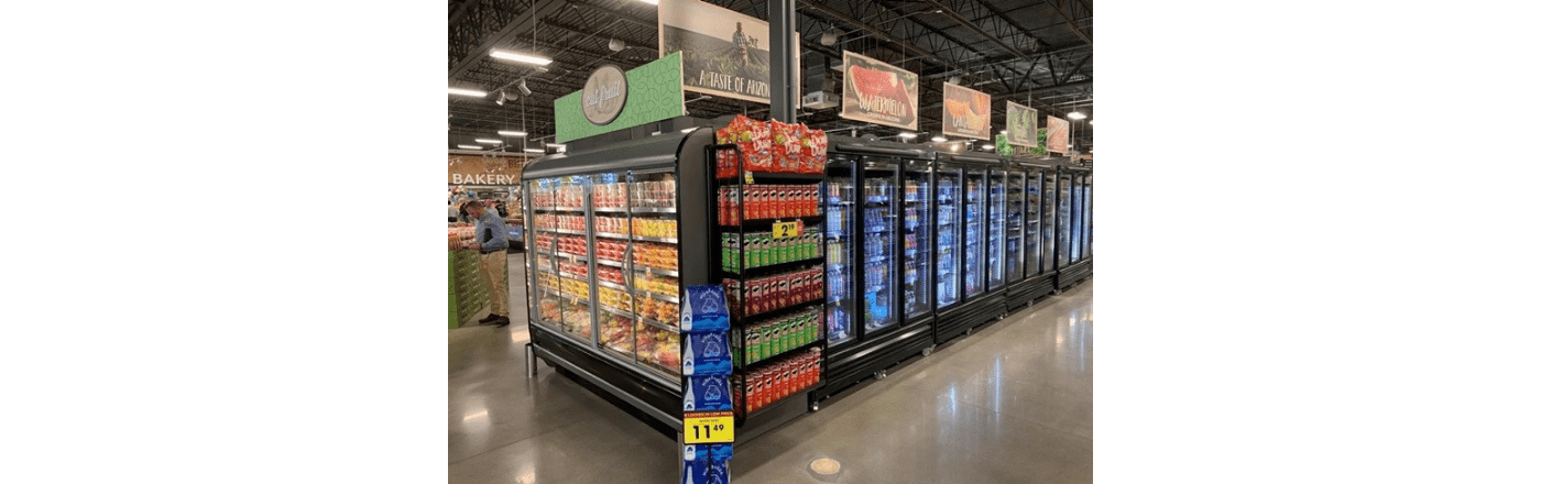 Refrigerated display units filled with colourful beverages and snacks in a grocery store aisle.