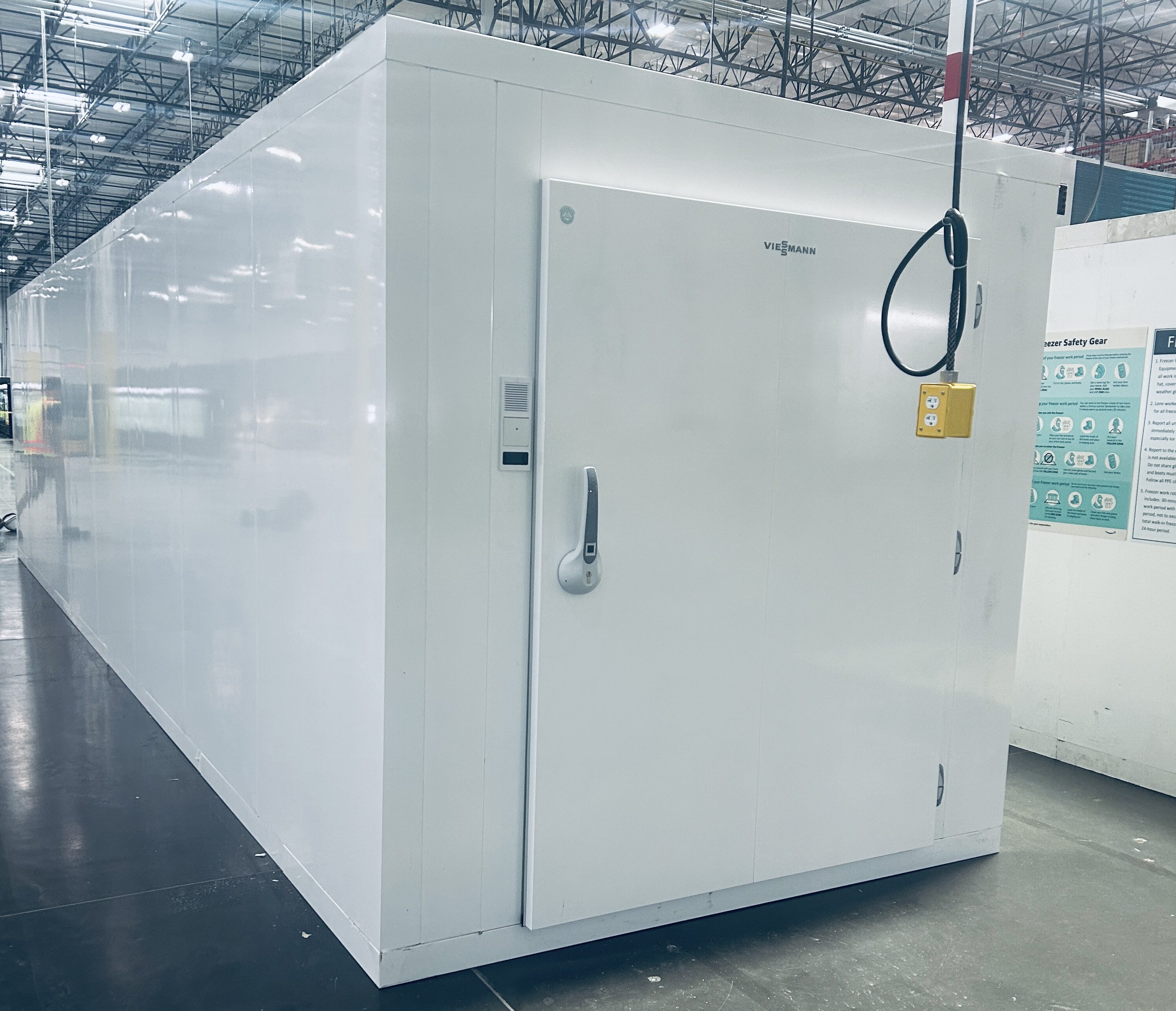 Large white refrigeration unit with a door, set against a grey floor in a commercial space.