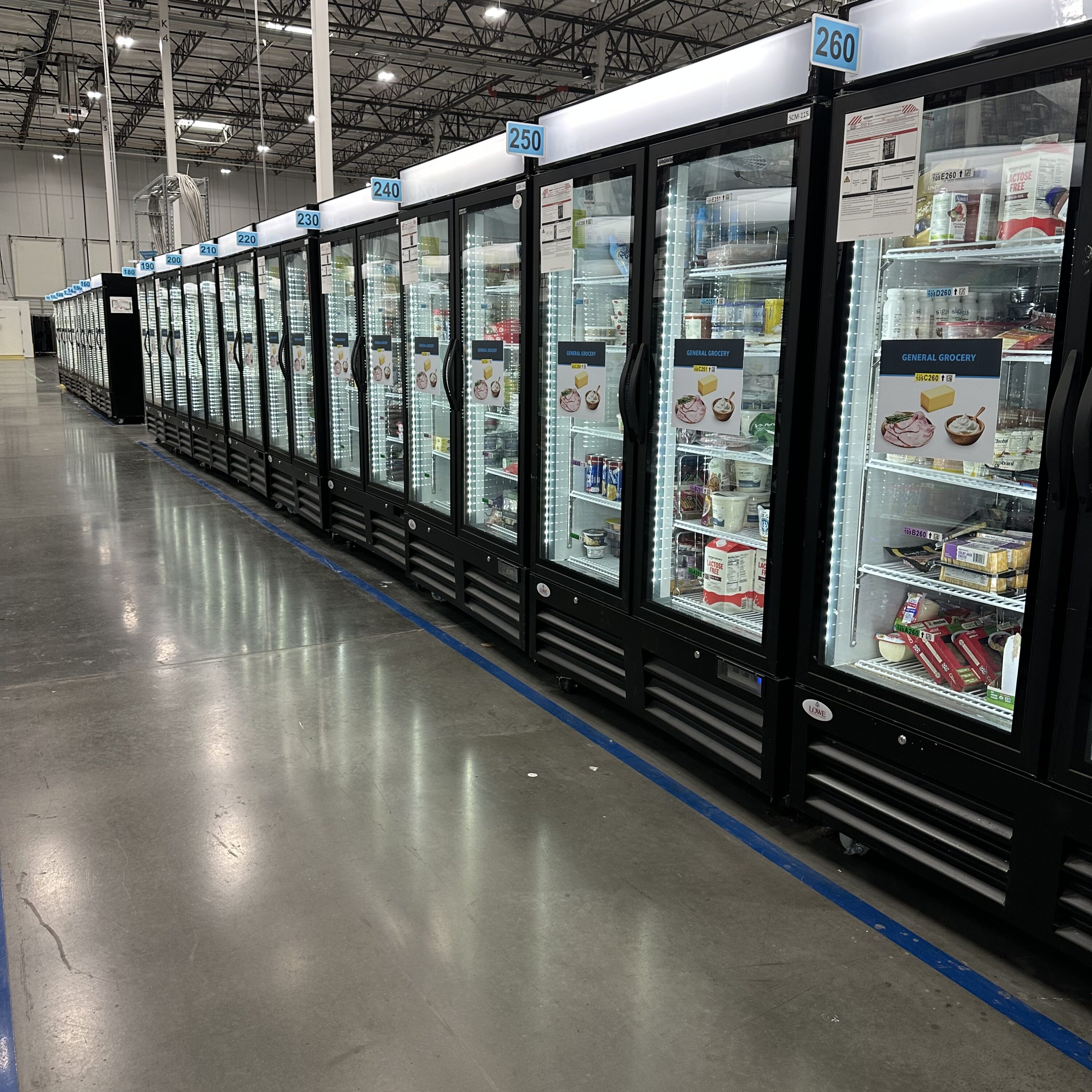 Row of black refrigeration units displaying various food products in a well-lit grocery store aisle.