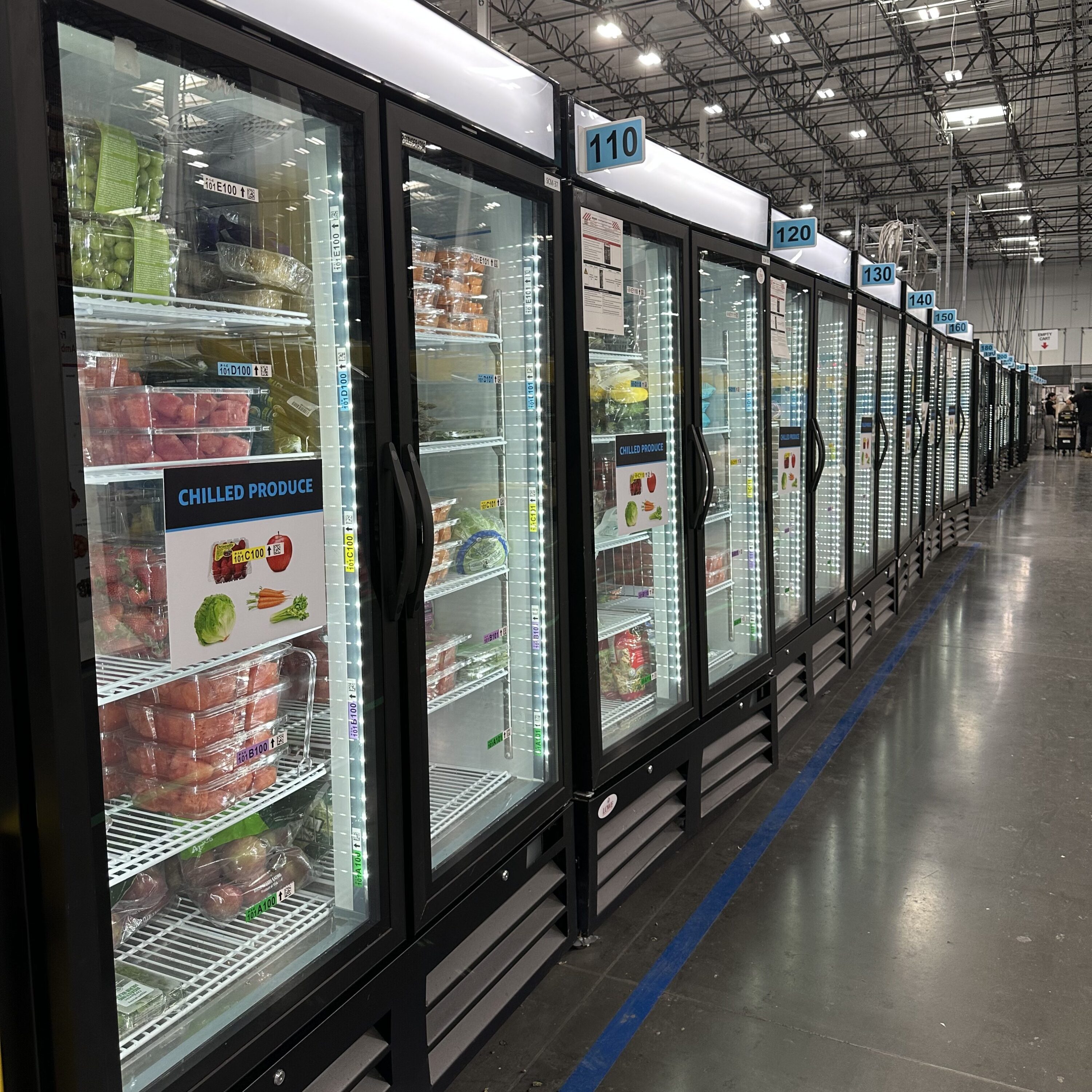 Rows of glass-fronted refrigeration cases displaying various food products in a retail environment.