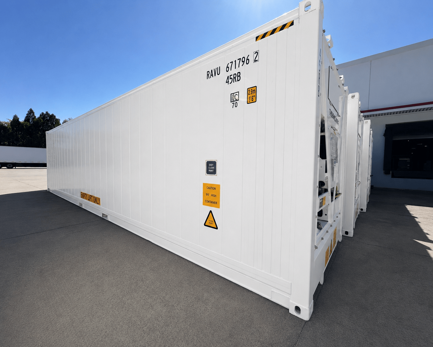 Large white shipping container with warning signs, set against a clear blue sky.