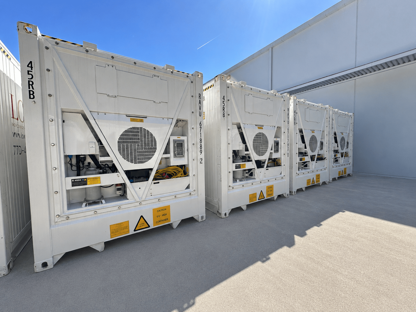 Four large white shipping containers with ventilation units, set against a clear blue sky.